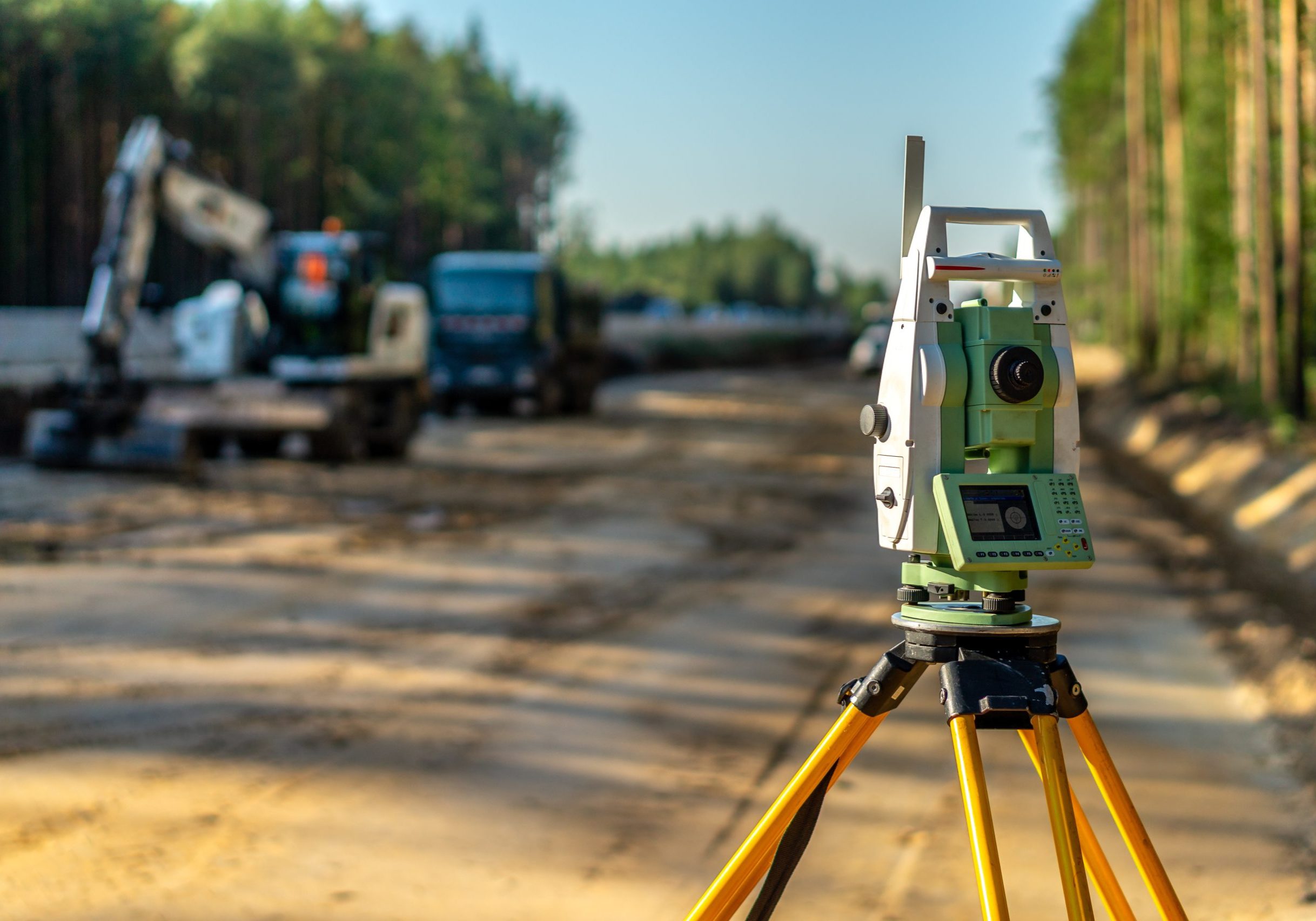 Surveyor engineer with equipment (theodolite or total positioning station) on the construction site of the road or building with construction machinery background